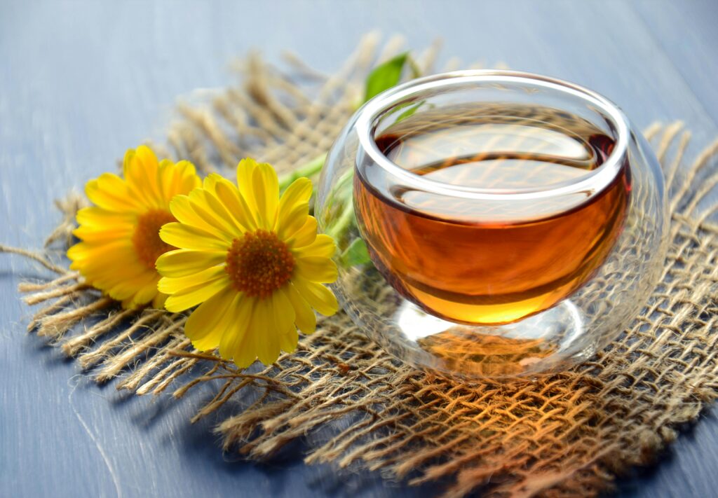 Glass cup of herbal tea with yellow flowers on a textured background.